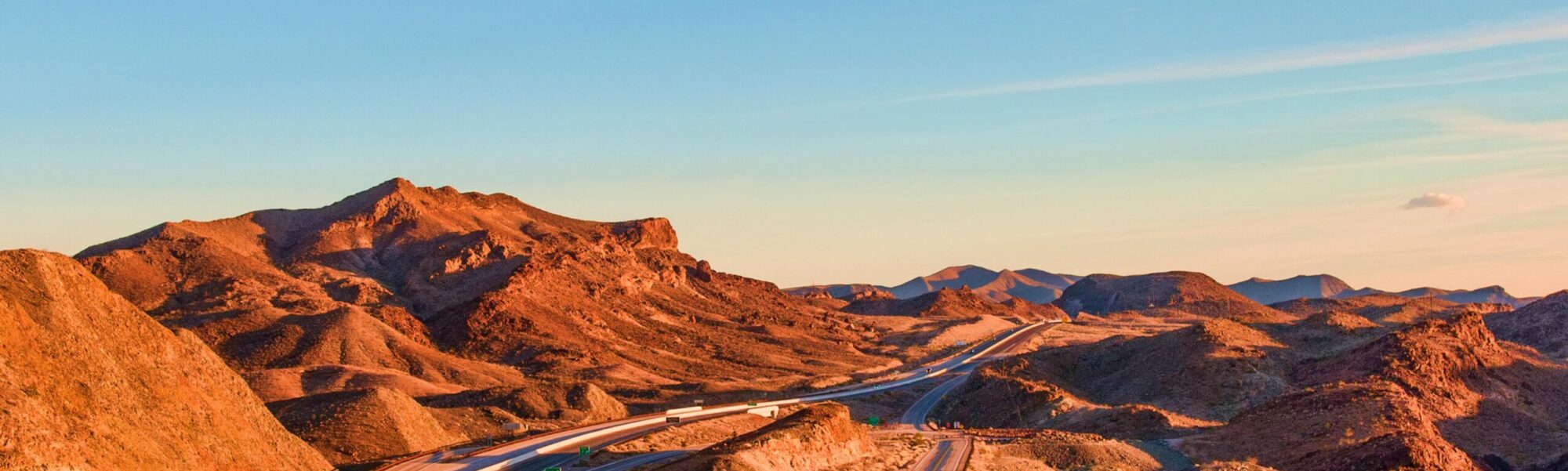 Stunning view of a winding highway amidst Nevada's rugged landscape under blue skies at sunset.